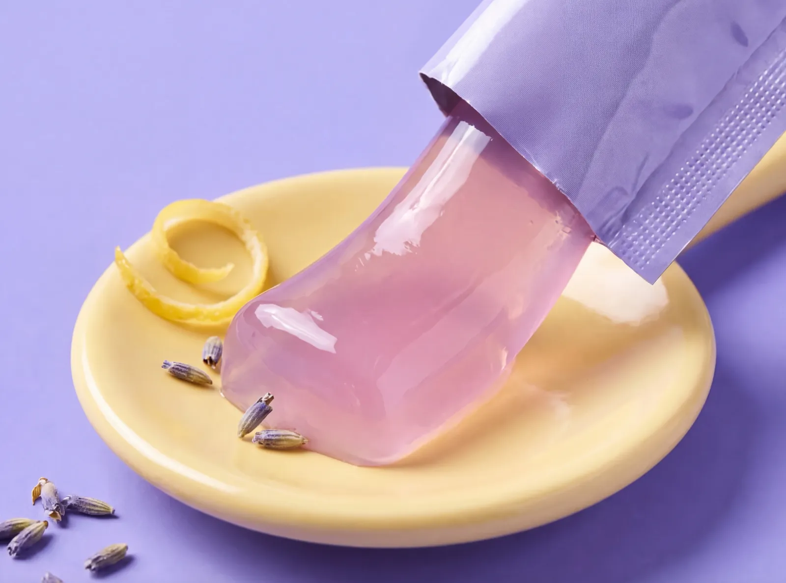 Pink jelly squeezed from a lilac stick onto a yellow dish with lemon peel and lavender